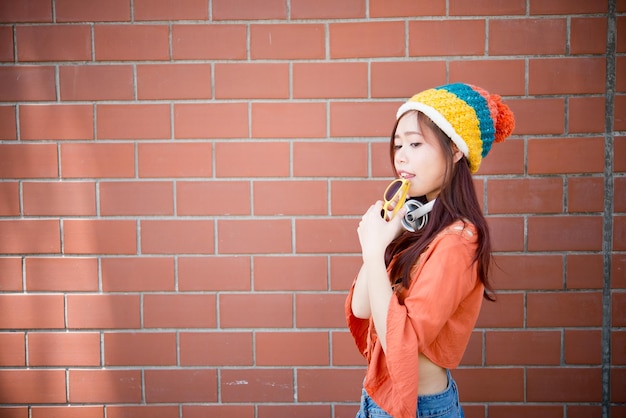 Chica asiática hipsters en pared de ladrillo naranja