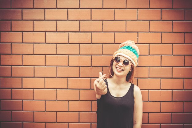 Chica asiática hipsters en pared de ladrillo naranjaestilo de vida de adolescente modernoFeliz dama posando para tomar una fotogente de tailandiagafas de sol naranjavintagefilm tone