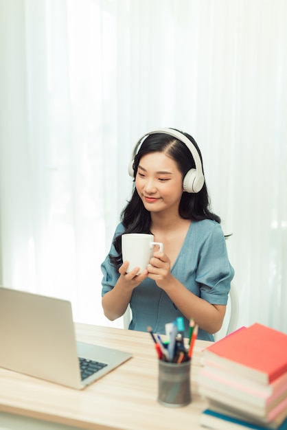 Chica asiática inteligente escritorio trabajo remoto portátil reloj seminario beber bebida taza en casa en el interior