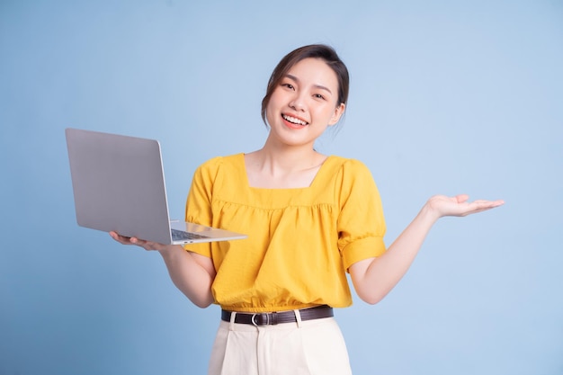 Chica asiática joven que usa la computadora portátil en fondo azul