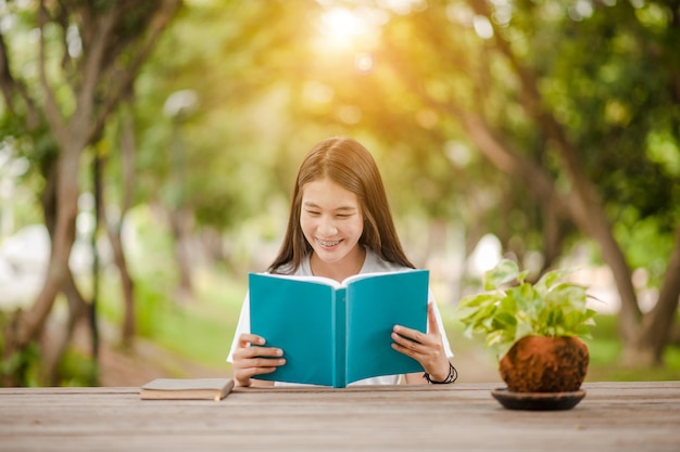 Chica asiática leyendo un libro en el parque en la luz del atardecer de verano Mujer asiática leyendo un libro en Tailandia Asia Hermosa mujer leyendo un libro en la mesa