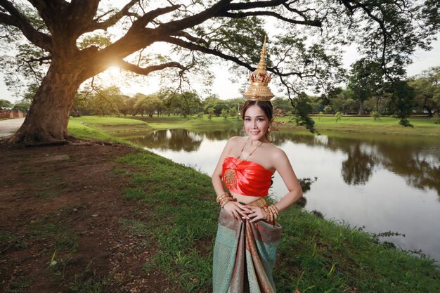 Chica asiática de moda en traje tradicional tailandés en templo antiguo con volante flor en mano y cara feliz