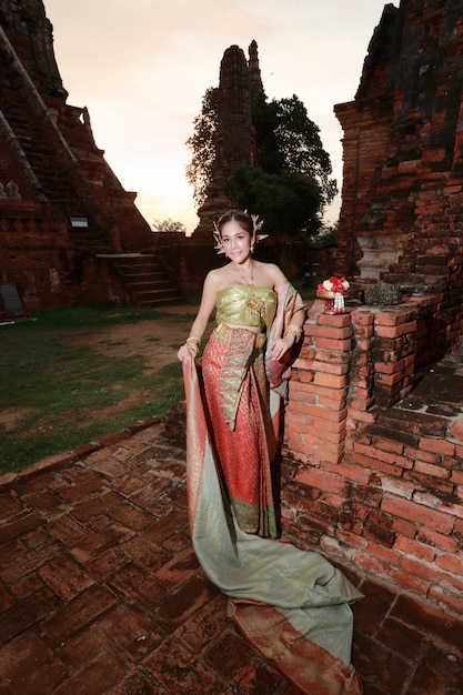 Chica asiática de moda en traje tradicional tailandés en templo antiguo con volante flor en mano