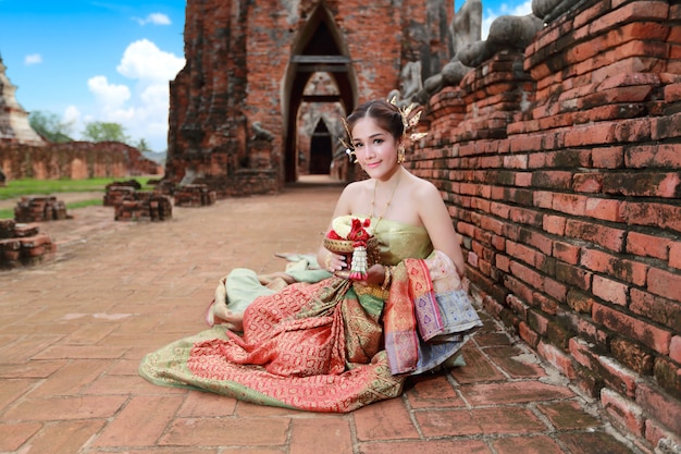 Chica asiática de moda en traje tradicional tailandés en templo antiguo con volante flor en mano