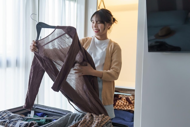 Chica asiática preparando vacaciones eligiendo ropa con armario en el dormitorio antes del viaje de vacaciones