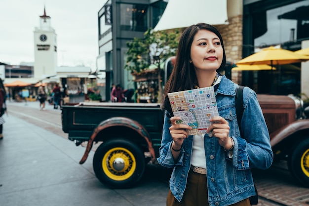 Foto una chica asiática que estudia en el extranjero con un mapa está mirando los alrededores en una camioneta. estudiante de intercambio con ganas de explorar nuevos lugares y probar cosas nuevas. estilo de vida autentico