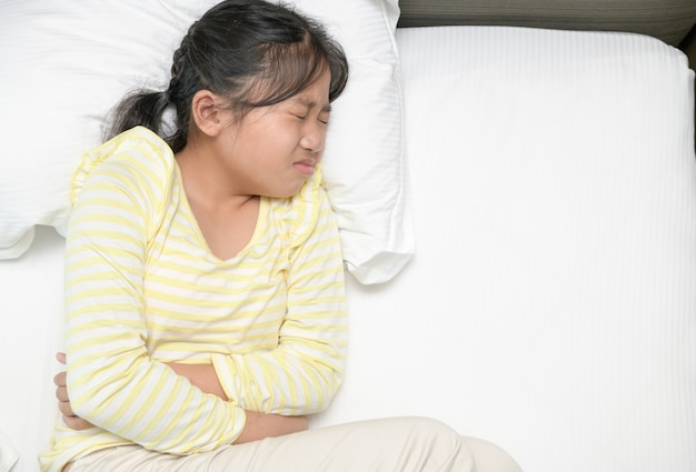 Chica asiática que sufre de dolor de estómago y está acostada en la cama. diarrea o concepto saludable