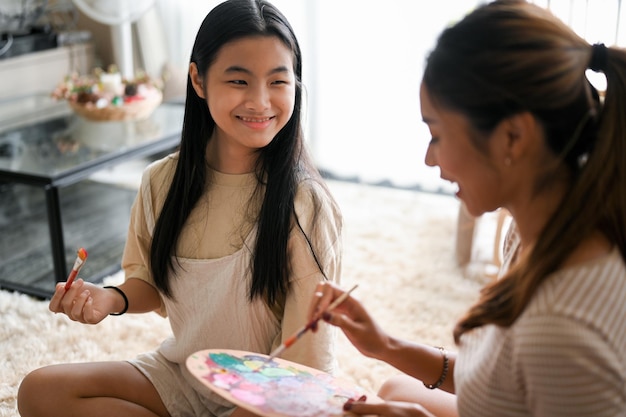 Una chica asiática sonriente disfruta hablando con su hermana mayor pintando juntos un cuadro creativo