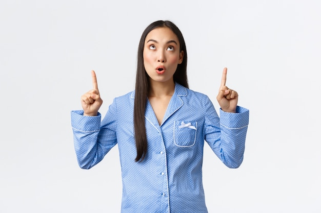 Chica asiática sorprendida e impresionada en pijama azul mirando y señalando con el dedo el banner promocional. Mujer en pijama se queda boquiabierta al ver un anuncio impresionante