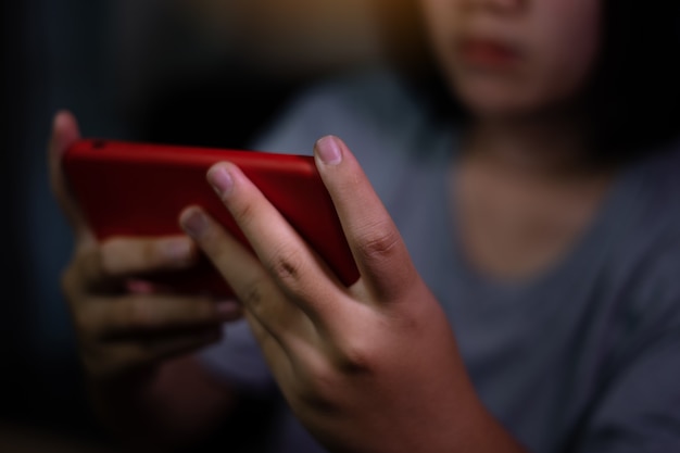 Chica asiática con teléfonos inteligentes o juegos móviles en el sofá en casa. Mujer joven con teléfono móvil en el sofá por la noche. Adicción al móvil o insomnio. Los jóvenes son un problema de adicción al teléfono.