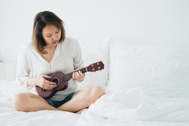 Chica asiática toca la guitarra desde la mañana despierta. haciéndolo sentir brillante