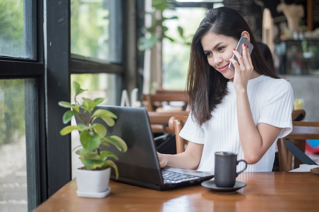 Chica asiática trabajando en cafetería con smartphone