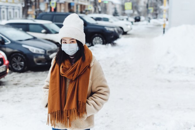 Chica asiática transeúnte en una máscara médica protectora al aire libre. Una mujer en la calle en invierno protege el tracto respiratorio de la epidemia de coronavirus