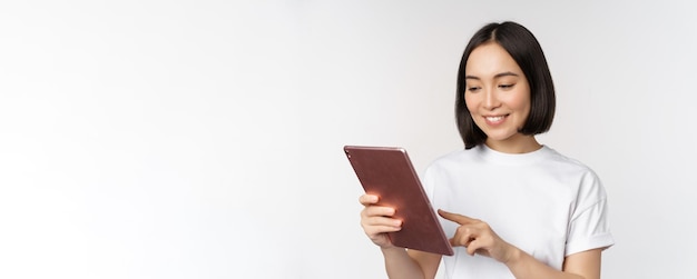 Chica asiática usando tableta digital trabajando con compras de gadgets en línea de pie sobre fondo blanco.