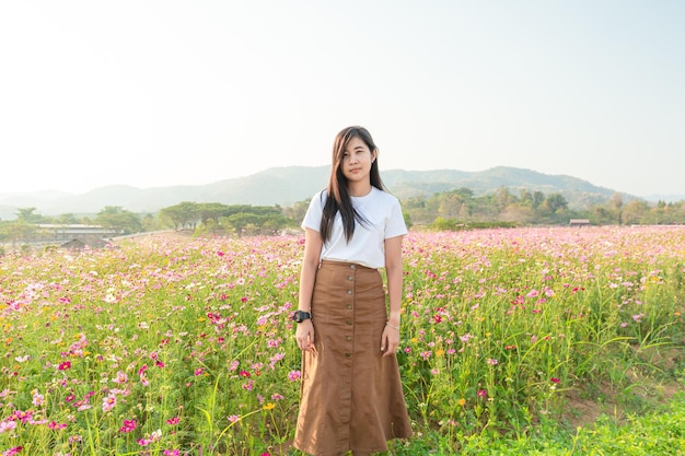 Chica asiática en vestido blanco se sienta en un prado de flores rosadas en el campo