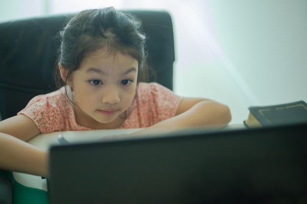 Chica asiática viendo escribir notas y mirar la computadora portátil en casa