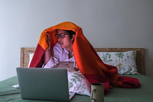Chica asiática viendo una película de terror en su computadora portátil con aspecto asustado
