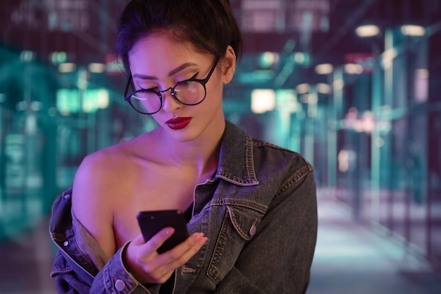 Chica Asina usando un teléfono inteligente en la ciudad por la noche.