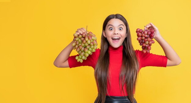 Chica asombrada sostiene racimo de uvas sobre fondo amarillo