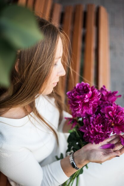 Chica de aspecto europeo con flores, peonías en sus manos.