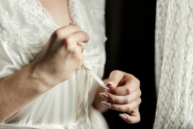 Chica ata el cinturón en su túnica de pie cerca de la ventana mujer preparándose antes de la ceremonia de la boda