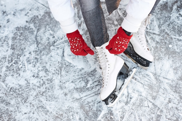 Chica atar cordones de los zapatos en patines de hielo antes de patinar en la pista de hielo, las manos en guantes de punto rojo.