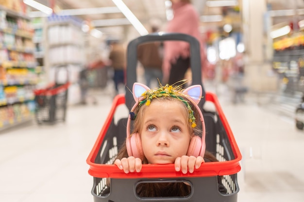 Una chica atenciosa con auriculares en el carrito de la compra en el supermercado