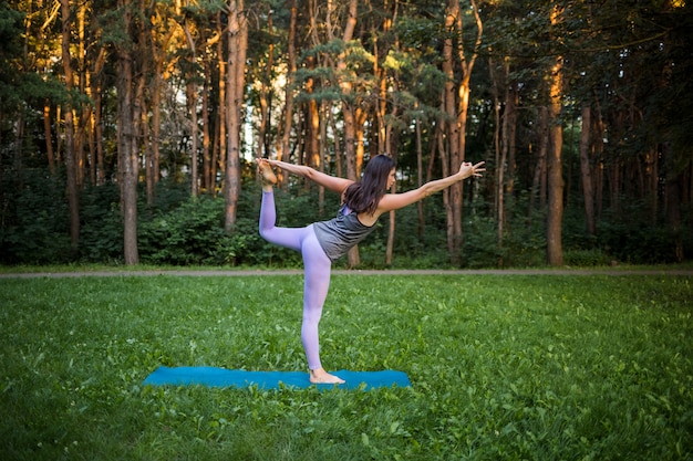 Chica atleta sobre una estera deportiva azul hace yoga en el bosque al atardecer