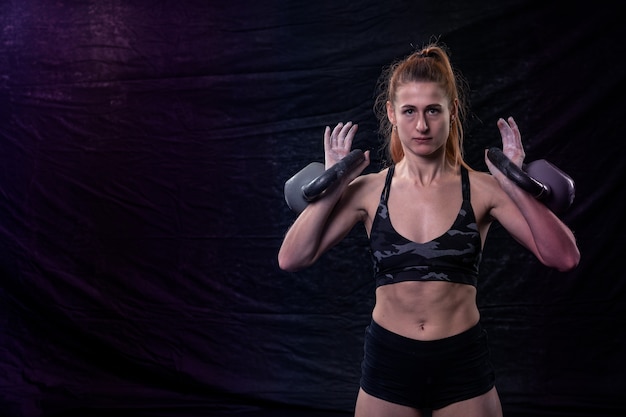 Foto chica atlética con cuerpo musculoso sosteniendo dos pesas en sus manos
