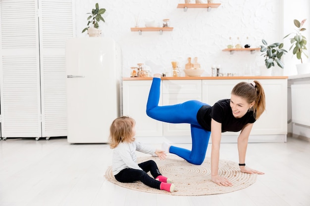 Chica atlética feliz e hija haciendo yoga en la cocina instructora de fitness mujer atractiva