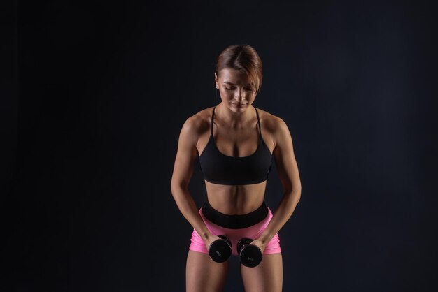 chica atlética haciendo ejercicio con pesas en fondo negro concepto deportivo