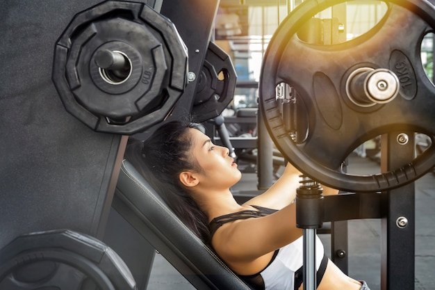 Chica atlética haciendo ejercicio con press de banca con barra inclinada en el gimnasio