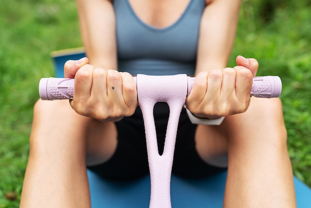 Chica atlética haciendo ejercicios en un entrenador de mano en la naturaleza al aire libre en un fondo borroso Una mujer está haciendo yoga en el parque sentada en el césped