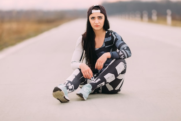 Chica atlética en ropa deportiva con aspecto brutal sentado en el asfalto