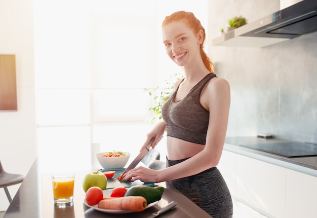 Chica atlética con ropa de gimnasia come fruta en la cocina