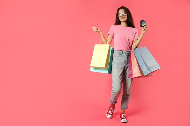 Chica atractiva con bolsas de papel multicolores sobre fondo rosa.