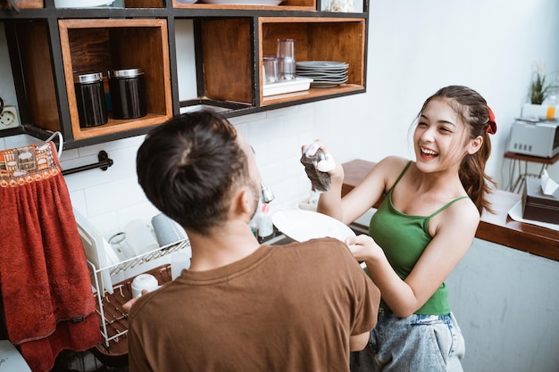 Chica atractiva bromeando con un joven mientras lava los platos juntos en la cocina