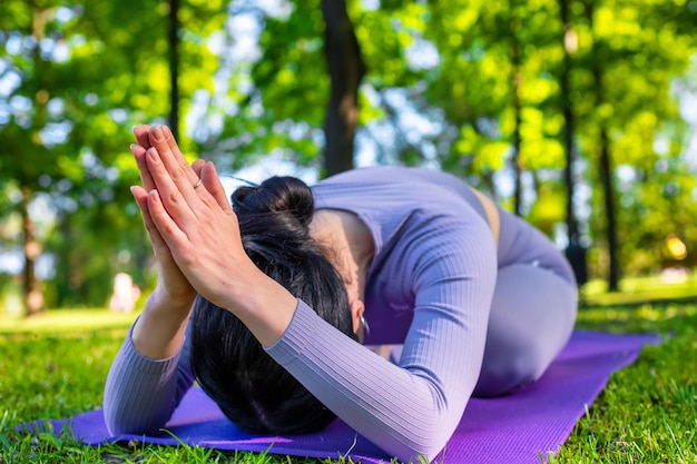 Chica atractiva con cabello largo y negro vestido de púrpura haciendo poses de yoga y meditando