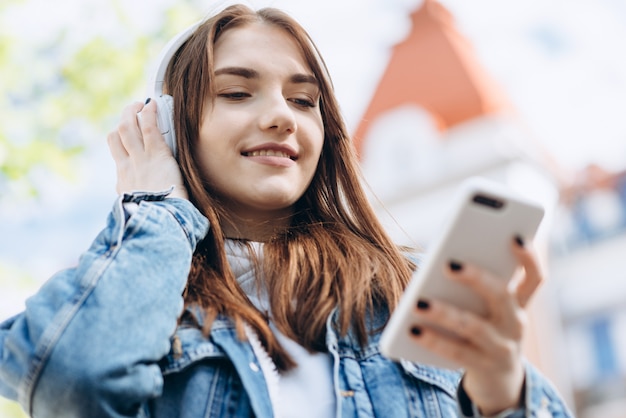 Chica atractiva con cabello oscuro y auriculares, mirando algo en el teléfono