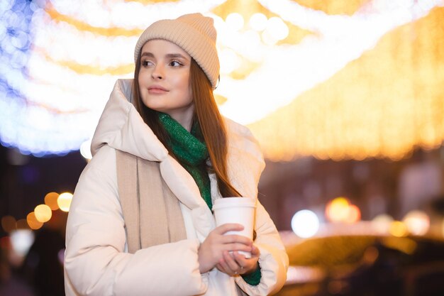 Chica atractiva caminando en la ciudad decorada con luces navideñas