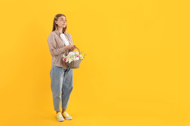 Chica atractiva con canasta de flores sobre fondo amarillo