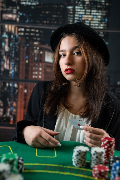 Chica atractiva con chaqueta y sombrero sosteniendo cartas de póquer y mirando a la cámara en el casino una mujer reparte cartas