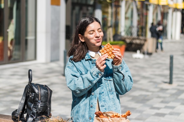 Chica atractiva comiendo con gran placer sabrosa comida de café para llevar en la calle. te lo mereces