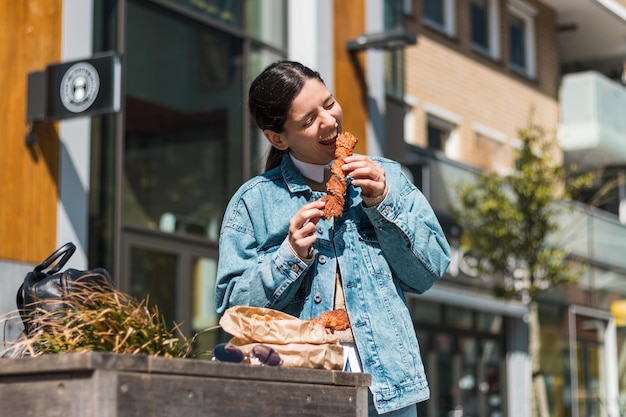 Chica atractiva comiendo con gran placer sabrosa comida de café para llevar en la calle. te lo mereces