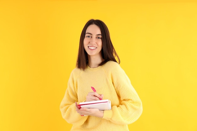 Chica atractiva con cuaderno sobre fondo amarillo