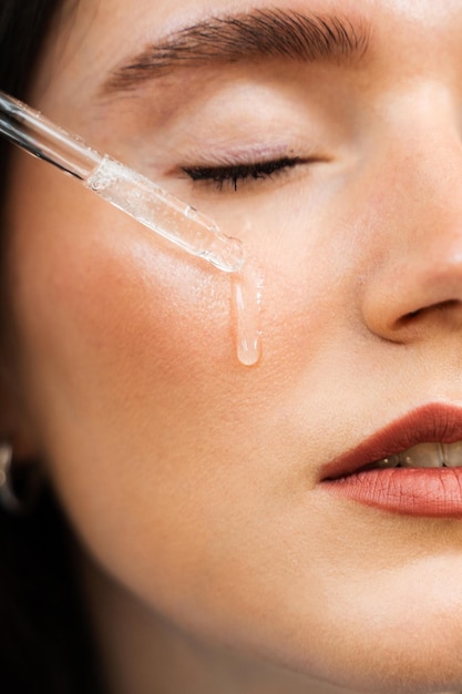 Foto una chica atractiva deja caer aceite esencial en la piel facial. una mujer joven se está aplicando un suero hidratante en la cara.