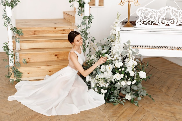 Chica atractiva elegante cerca del piano con flores