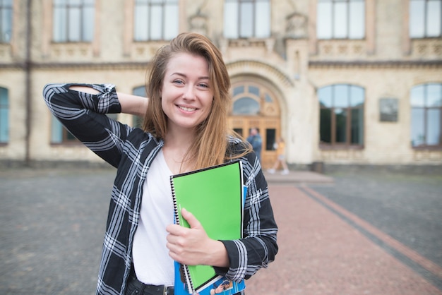 Chica atractiva estudiante con libros y cuadernos en sus manos pone una cámara en el