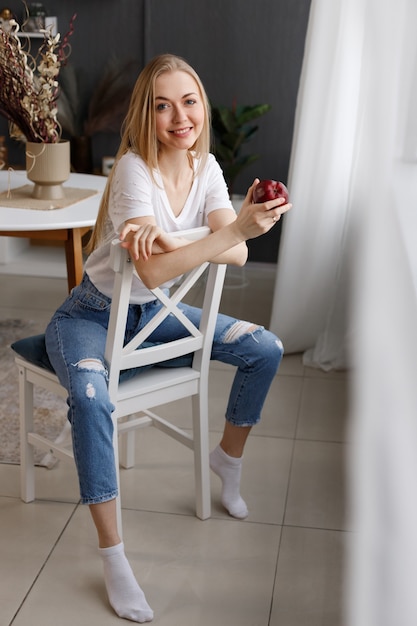 Chica atractiva con una manzana sentada en una silla en casa