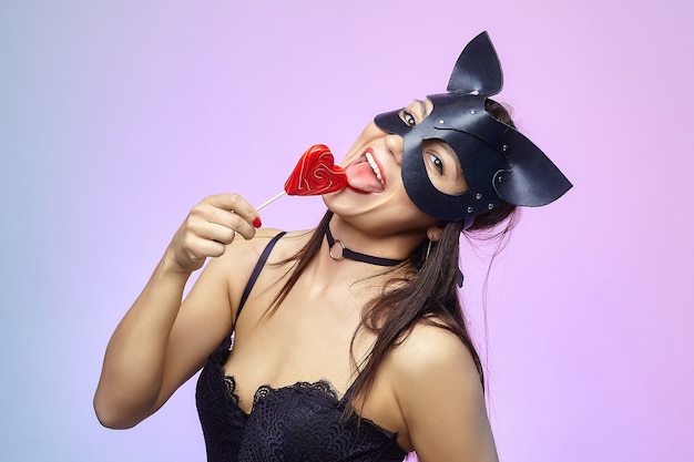 Chica atractiva en máscara de gato lamiendo dulces.